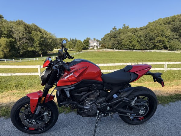 Red 2026 Ducati Monster+ parked by a white fence